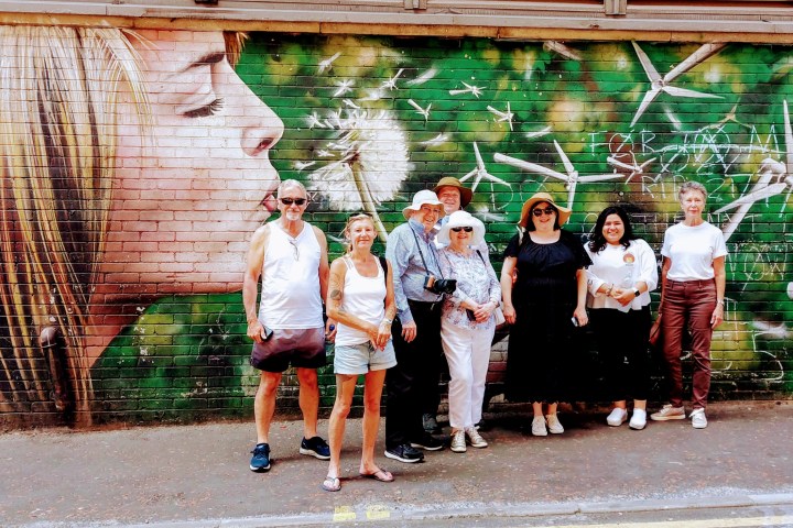 Group of people posing in front of mural with woman blowing dandelions.