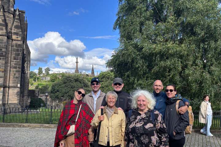 Group of seven people smiling in front of historic buildings and trees.