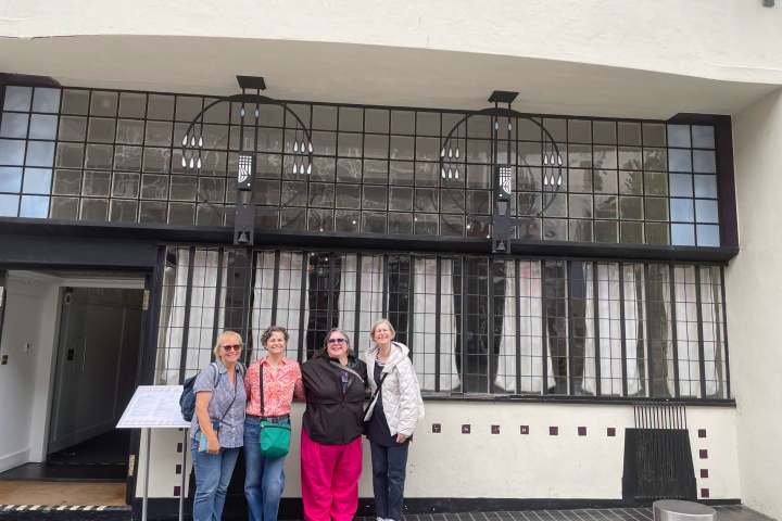 Four people posing in front of a building with large windows.