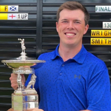 Smiling person holding a trophy in front of a scoreboard.