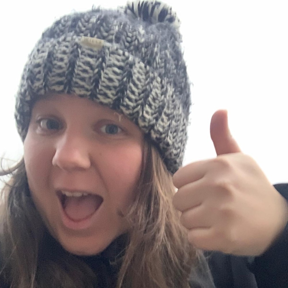 Person in knit hat giving a thumbs up with an open-mouthed smile.
