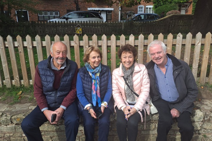 Four people sitting on a bench in front of a wooden fence, smiling.