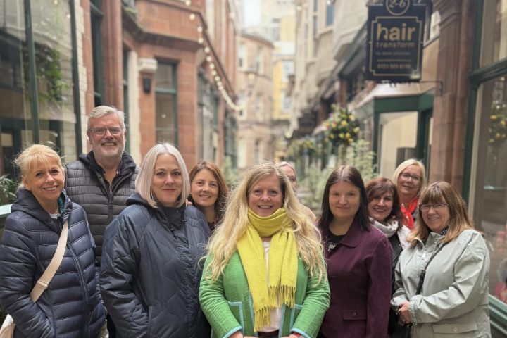 Group of nine adults posing in a narrow street with shops.