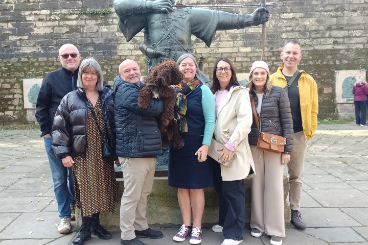 Group of people and a dog pose by a statue of a historical archer with a bow.