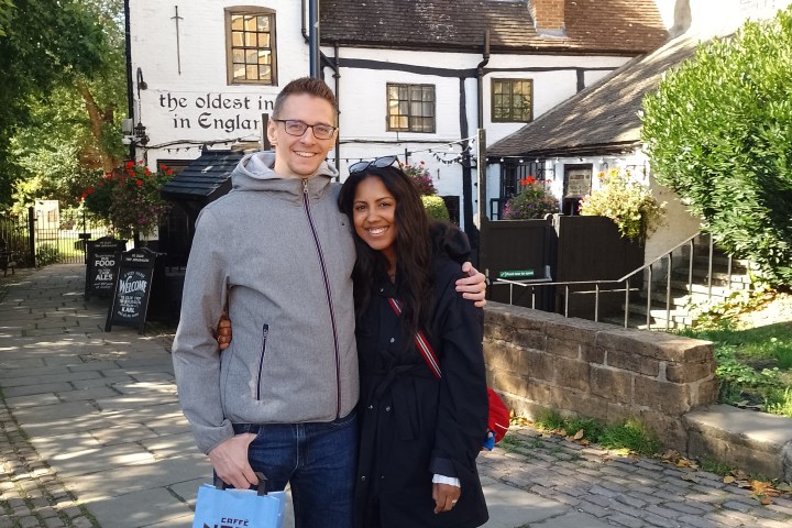 Two people posing in front of a historic white pub building with old signage.