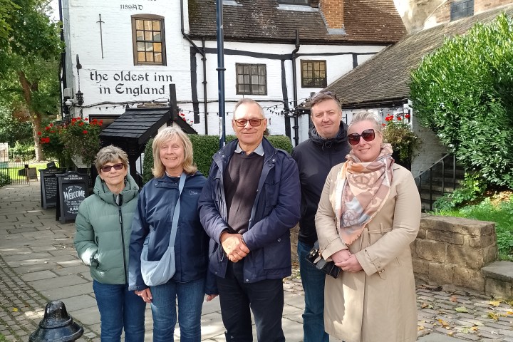 Five people stand in front of an old inn labeled 'the oldest inn in England' with historical architecture.