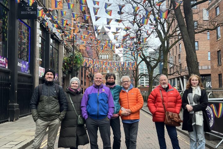 Group of people posing under rainbow flags on a city street.