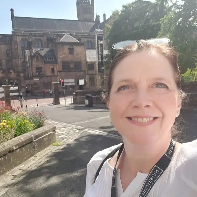 Smiling person taking a selfie with a historic building in the background.