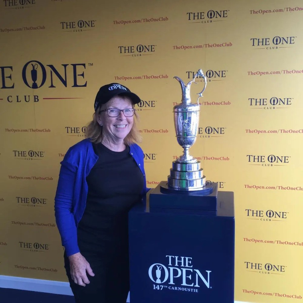 Person wearing a cap, standing next to a trophy at The Open 147th Carnoustie backdrop.