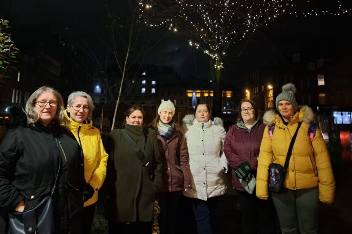 Group of seven people in winter coats under a tree with lights at night.