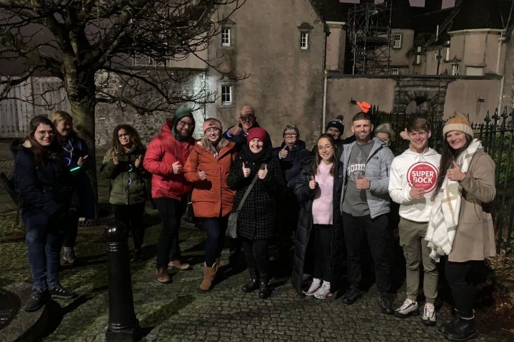 Group of people posing outdoors at night in front of a historic building.