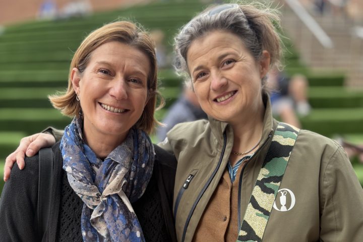 Two smiling women posing together arm in arm outside on steps.