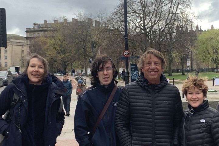 Four people standing outdoors with trees and buildings in the background.