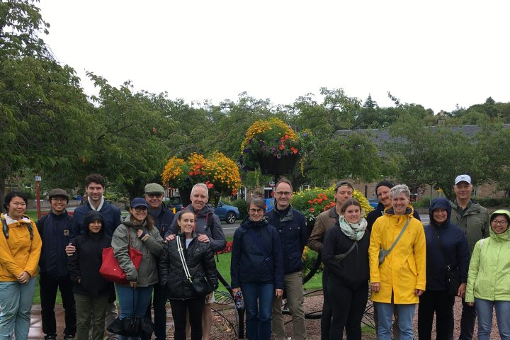A group of people in raincoats standing on a path in a park with lush greenery and hanging flowers.