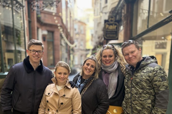 Group of five people smiling in a narrow street with historic buildings.