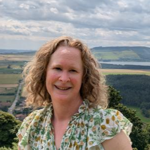 Smiling person in floral top with scenic landscape in background.