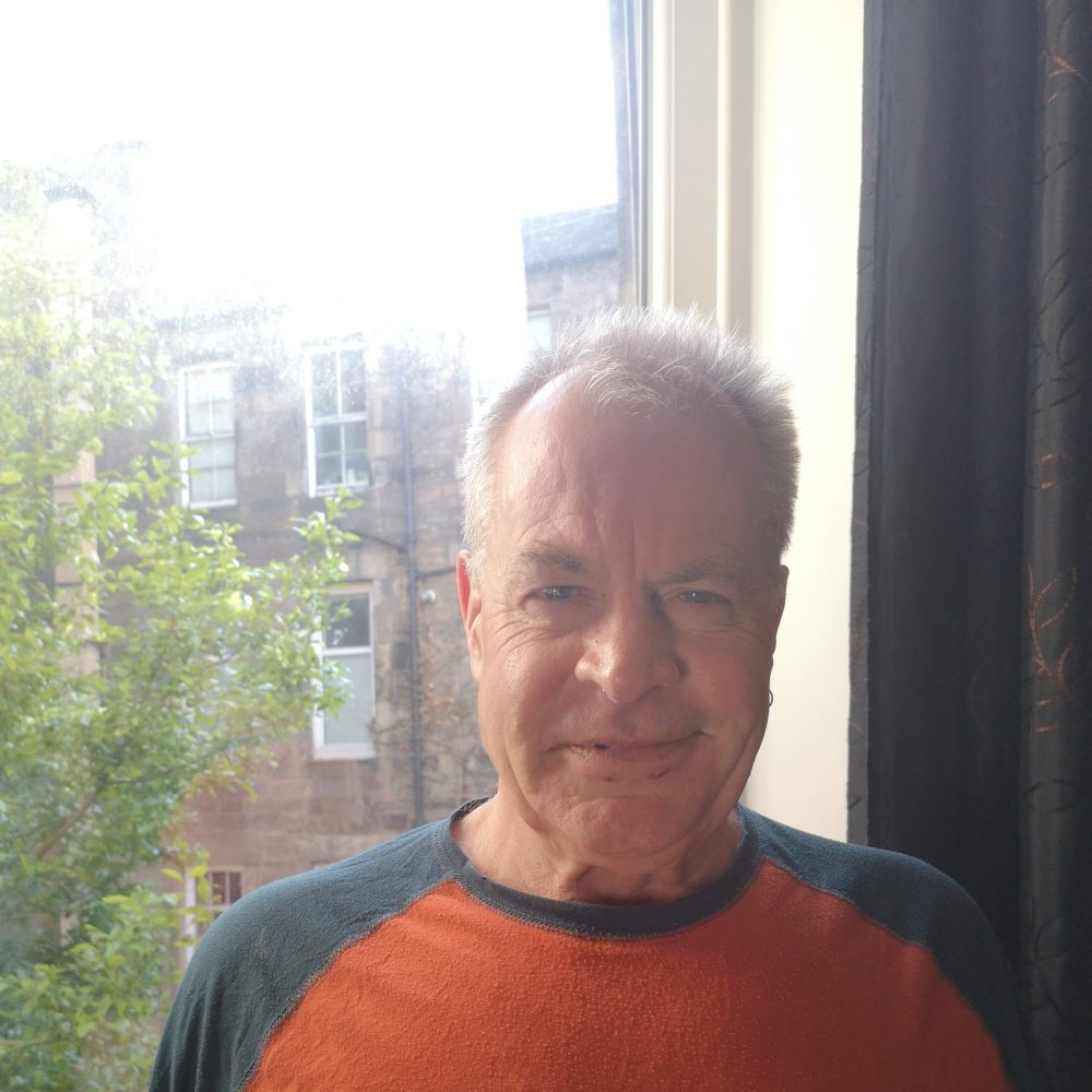 a man in orange shirt sitting in front of a window