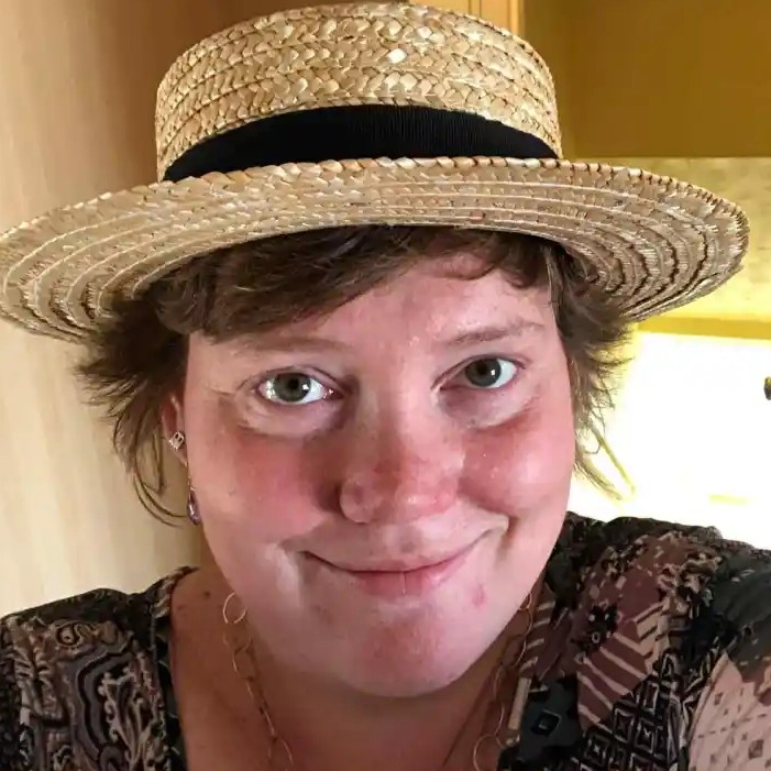 Person wearing a straw hat and patterned shirt, smiling indoors.