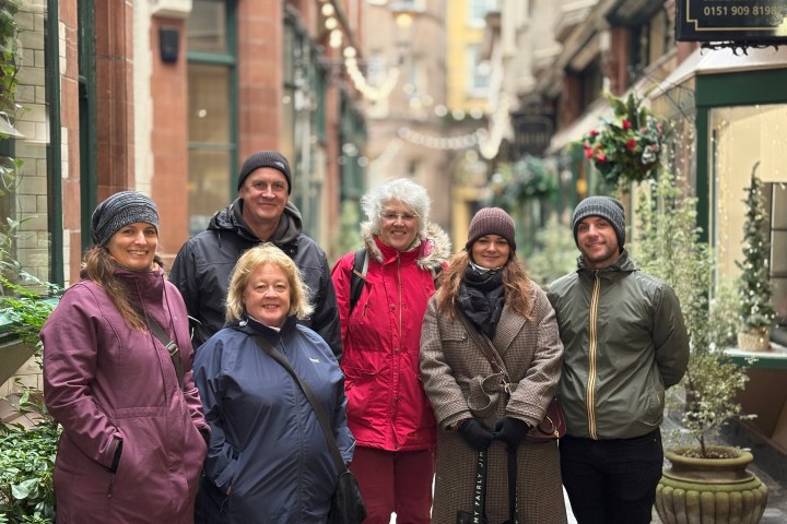Six people in warm clothing pose in a narrow alley with festive decorations.