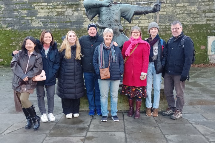 Group of seven people posing in front of a statue with an archer in a courtyard.