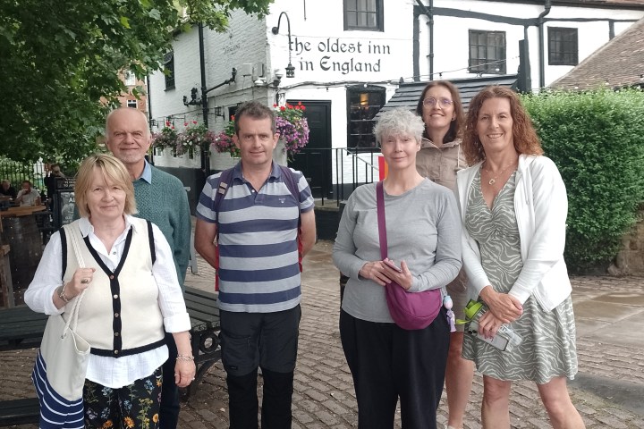 Six adults standing on cobbled street in front of a historic inn with foliage overhead.
