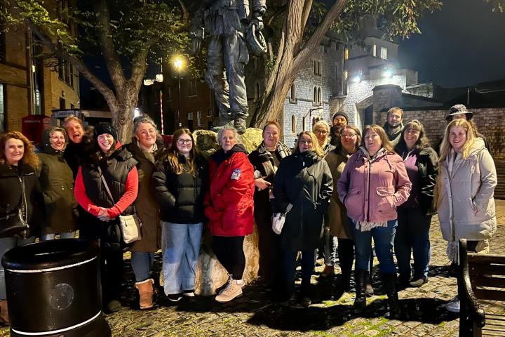 Group of people standing by a tree and statue on a cobblestone street at night.