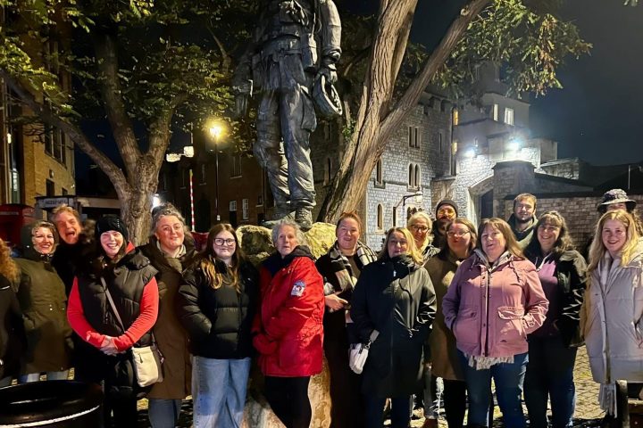 Group of people posing by a statue on a cobblestone street at night.