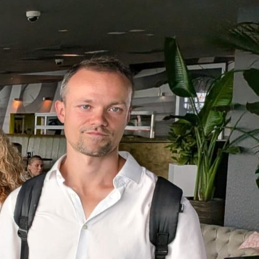 Man in white shirt with backpack in a modern indoor setting with plants.