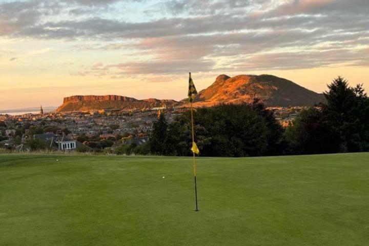 Sunset view of a golf course green with distant hills and a cityscape.