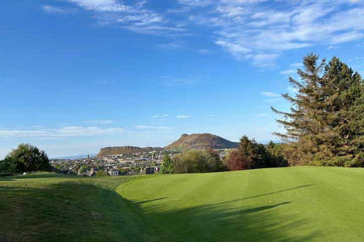Green golf course with distant hills, trees, and a clear blue sky.