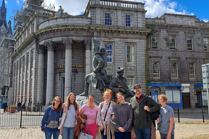 Group of people posing in front of a historic building with statues under a blue sky.