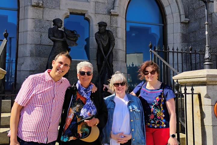 Four people smiling in front of a stone building with statues and arched windows.