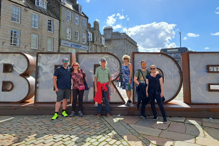 Six people standing in front of large 'ABERDEEN' letters on a sunny day.