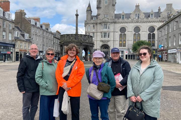 Group of six people posing in front of a historic building with a gothic architectural style.