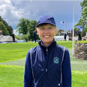 Person smiling in a navy cap and jacket on a golf course with a cloudy sky.