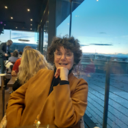 Smiling person seated in a cafe with evening sky in the background.