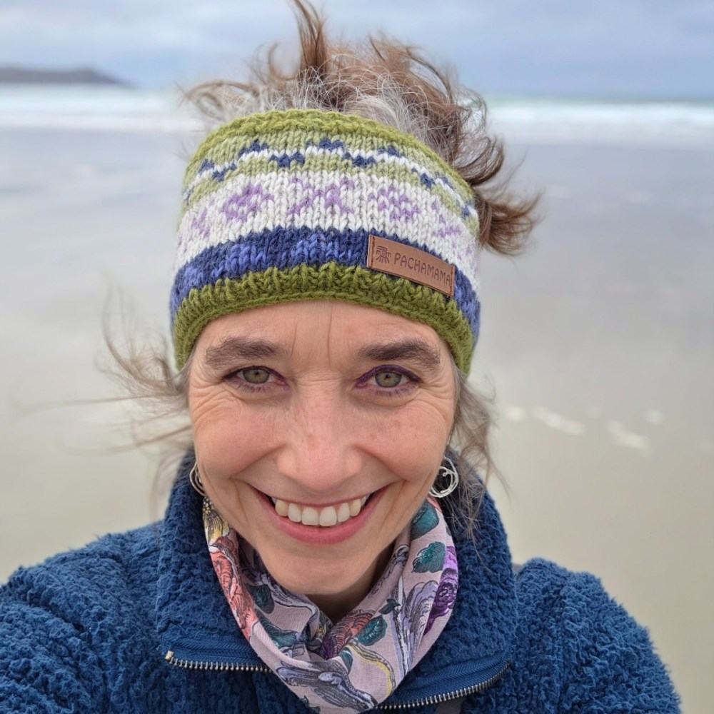 Person with headband smiling on a windy beach.